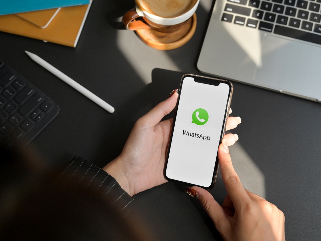 Persona utilizando su celular. En la pantalla se ve el logo de WhatsApp. 