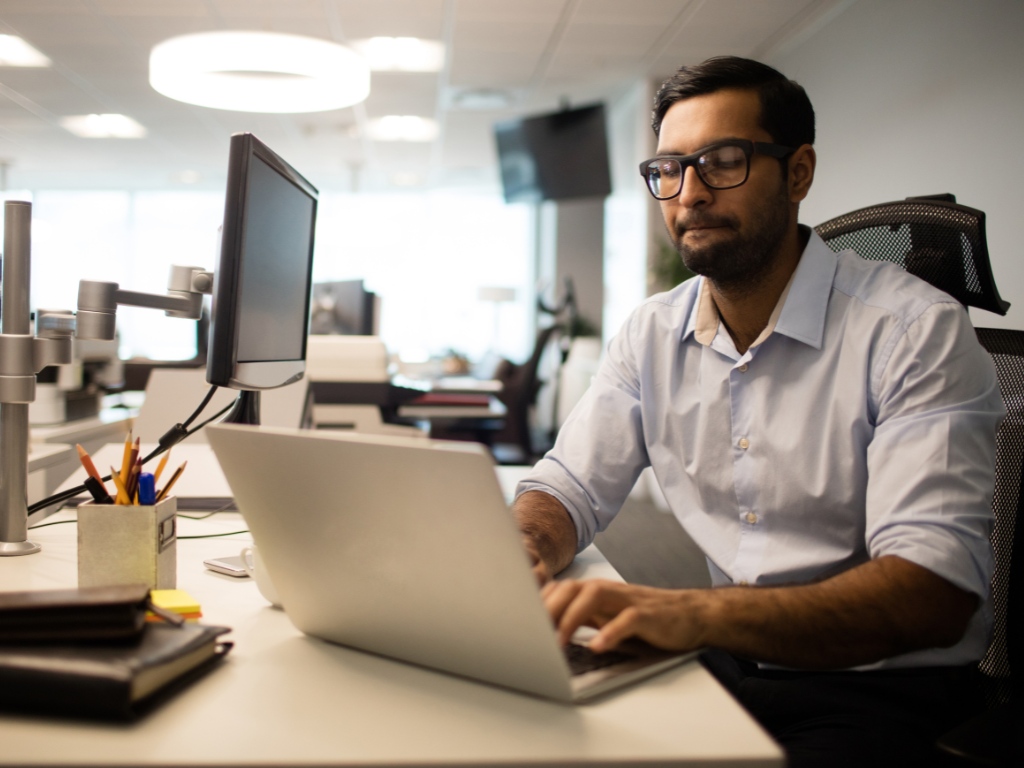Hombre a cargo de una pyme, con una expresión de concentración y determinación, se inclina sobre su computador, busca en él cómo automatizar los procesos de su negocio.