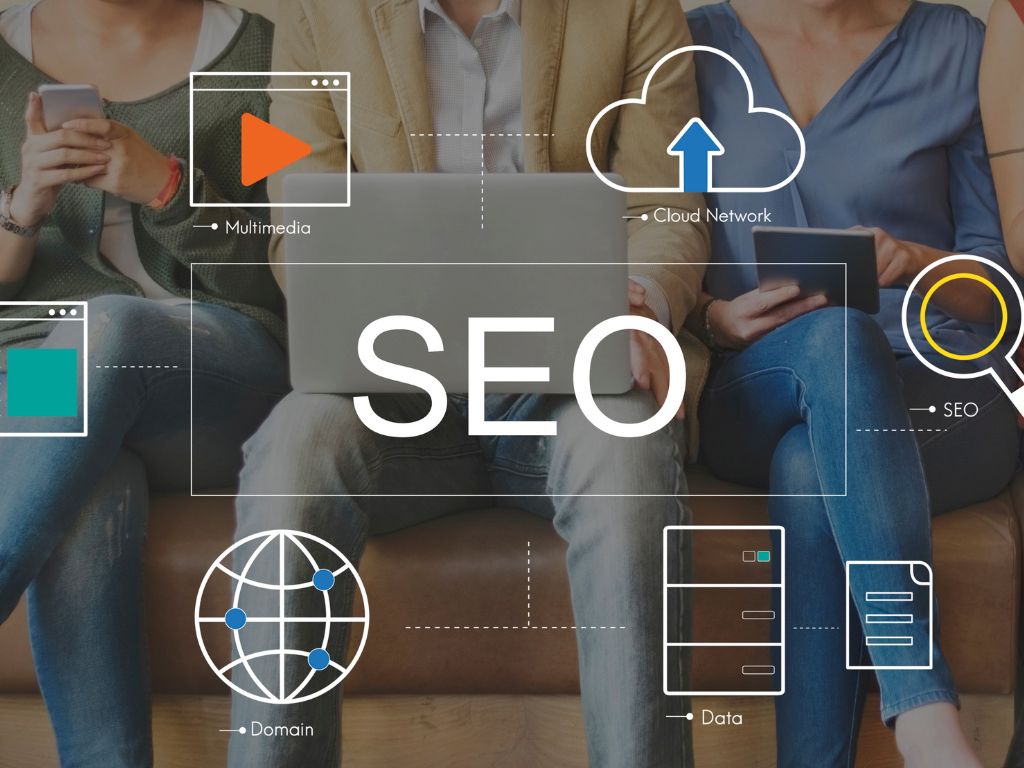 Grupo de personas sentadas, cada una usando un dispositivo digital como un computador o un teléfono móvil. Alrededor de ellas, hay varios íconos que representan conceptos relacionados con el marketing digital y las estrategias de posicionamiento SEO. 