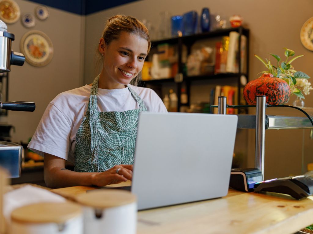 Joven dueña de una pequeña cafetería se encuentra buscando cómo hacer marketing para pequeños negocios en su computador. 