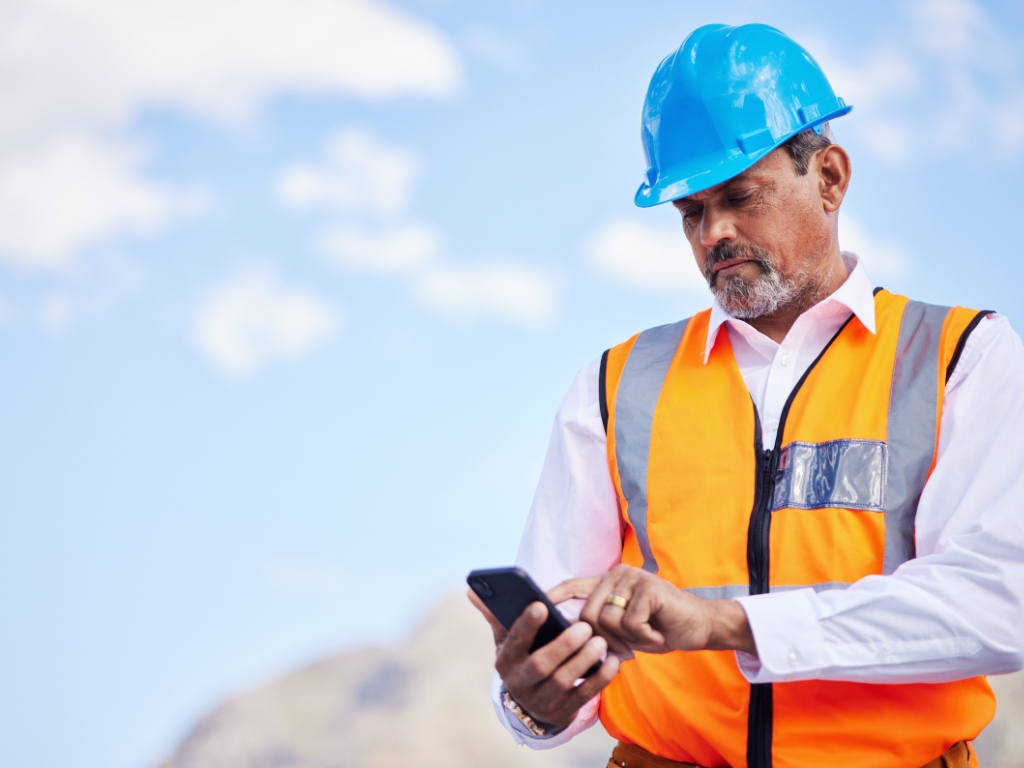 Trabajador en terreno utilizando su teléfono móvil para enviar un SMS en zona sin cobertura, representando comunicación satelital en operaciones remotas.