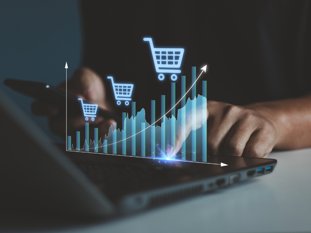 Gráfico de crecimiento de ventas online con íconos de carrito de compras sobre una computadora, simbolizando el aumento de ventas durante el Cyberday.