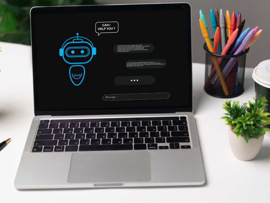 Computador con pantalla que muestra una interfaz de chatbot, representando el concepto de marketing conversacional, con herramientas de oficinam como un portalápices y plantas pequeñas al lado. 